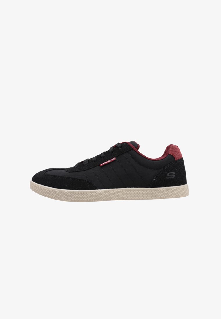 Zapatillas negras con parte superior de ante y textil, acentos rojos en el talón y la lengua, suela de goma texturizada y detalles de costura horizontal.