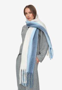 Zachte wolschal met een verloop van wit naar lichtblauw naar donkerblauw, met franjes aan de uiteinden. De textuur lijkt gezellig en warm.
