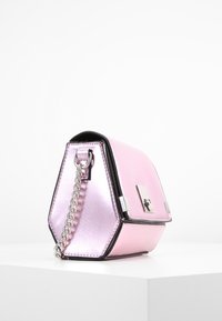 Borsa a mano esagonale rosa con una finitura metallica, dettagli neri, tracolla in catena argentata e chiusura a scatto. Superficie con finitura testurizzata.