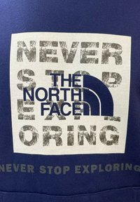 Felpa blu navy con testo grafico audace in bianco e grigio: "NON SMETTERE MAI DI ESPLORARE" e "THE NORTH FACE" con dettaglio del logo.
