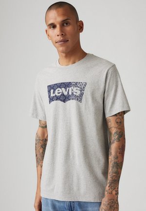 Camiseta de algodón gris con un gran estampado gráfico en azul marino que incluye el texto "Levi's". Diseño de mangas cortas y cuello redondo.