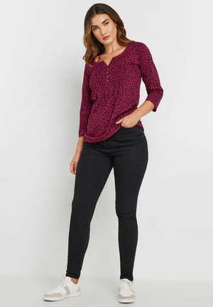 Blouse magenta à imprimé léopard noir, avec un décolleté rond et des manches trois quarts, assortie à un jean slim noir et des baskets blanches.