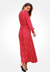 Vestido maxi floral rojo con mangas largas, cintura ceñida y falda fluida. Presenta pequeñas flores blancas sobre un fondo brillante.