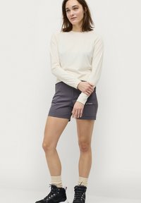 Langarmige crèmekleurige top in combinatie met grijze shorts. De outfit is gemaakt van een soepele, lichtgewicht stof, met zichtbare stiksels en zakken.