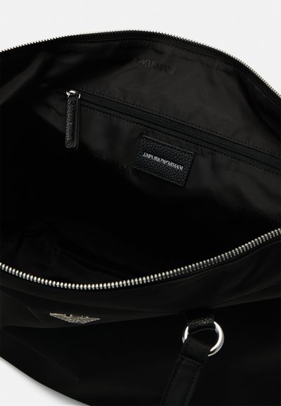 Borsa a tracolla nera con un esterno liscio, zip argentata e patch del logo. L'interno presenta una tasca con zip e foderatura morbida.