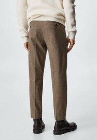 Ruskeat ruutukuosiset housut, joissa on muotolaskettu malli, kahdella takataskulla ja sileällä pinnalla, yhdistetty mustiin nilkkabootseihin.