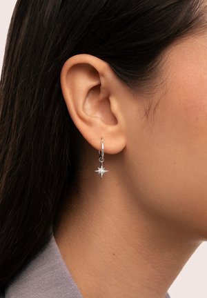 Silberne Creole mit einem sternförmigen Anhänger und einem zentralen Edelstein, präsentiert mit einer polierten Metalloberfläche und einem eleganten Design.