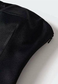 Primo piano di una manica in satin o seta nera caratterizzata da una cucitura e un piccolo tirante zip nero su uno sfondo bianco.