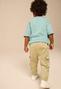  világoskék, rövid ujjú póló, bézs cargo nadrággal, oldalsó zsebekkel, fehér sportcipővel és rugalmas mandzsettákkal.