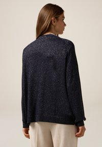 Granatowy sweter dzianinowy z metalicznymi akcentami, charakteryzujący się luźnym krojem, długimi rękawami oraz ściągaczami na mankietach i u dołu. Teksturowane wykończenie w całej powierzchni.
