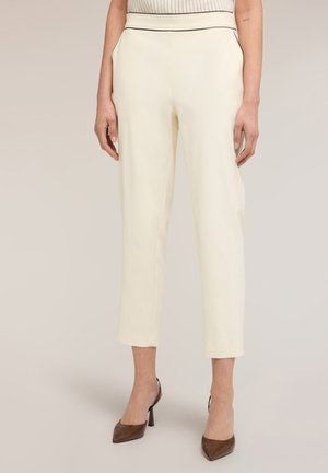 Kvinde iført højtaljede, cremefarvede cropped bukser med tætsiddende talje og brune spidse højhælede sko.