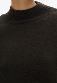 Pull noirâtre avec un col montant côtelé. Le tissu semble doux avec une finition texturée et un design en maille lâche.