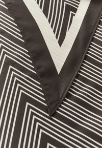 Zwart-wit stof met geometrische zigzag- en V-vormige patronen, met gedetailleerd stikwerk op het puntige V-gedeelte.