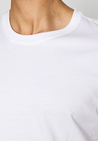 Camiseta blanca de algodón con un escote redondo. La tela parece suave y lisa, mostrando un diseño simple y clásico sin estampados.