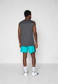 Un débardeur gris à coupe décontractée, associé à un short teal vif. Des chaussettes de sport blanches et des chaussures complètent le look sportif.