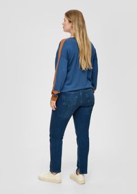 Sudadera azul con detalles de rayas marrones, combinada con vaqueros de mezclilla oscuros y zapatillas blancas. El conjunto presenta un ajuste casual y un estilo relajado.