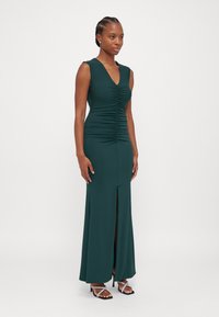 Green, sleeveless long dress with a deep V-neck and ruched detailing. Features a side slit, smooth texture, and a fitted silhouette.