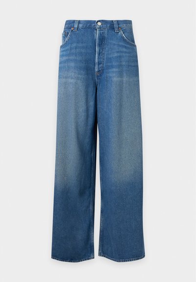 Jean denim bleu à jambes larges avec un lavage délavé, fermeture devant par bouton et zip, et deux poches avant visibles.