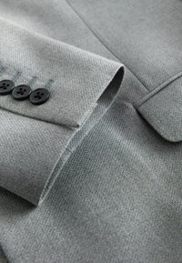 Gray textured fabric of a suit jacket with a folded lapel, featuring four black buttons and subtle stitching detail.