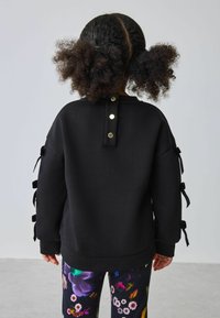 Felpa nera con dettagli a nastri sulle maniche e bottoni automatici dorati sul retro, abbinata a leggings con stampa floreale colorata.