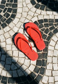 Tongs rouges posées sur un pavement en mosaïque de pierre noir et blanc avec un motif circulaire sous un soleil éclatant.