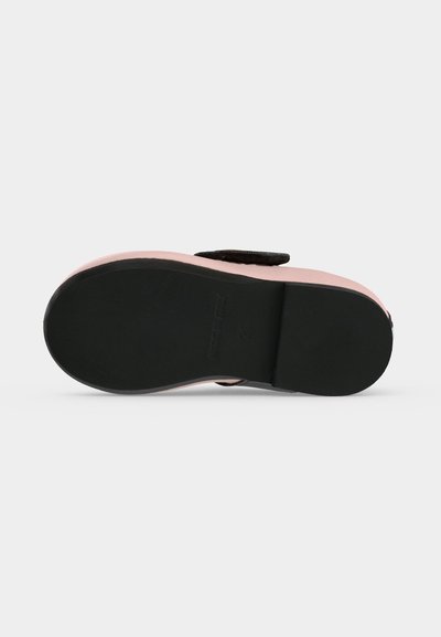 Chaussure rose d’enfant avec semelle noire vue par le dessous, montrant une semelle lisse et une seule bride sur le dessus.