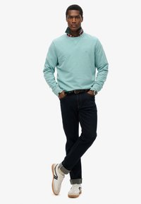 Lichtblauwe sweatshirt over een geruit shirt, gecombineerd met donkere spijkerbroek en witte sneakers met zwart en grijs accent.