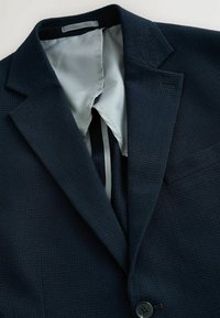 Marinefarbener Blazer mit Struktur, Reverskragen, einem Knopfverschluss und einem hellgrauen Satinfutter. Verfügt über eine Brusttasche und Innendetails.
