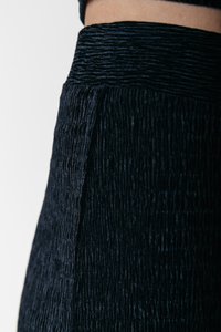 Material texturat negru cu un model zbârcit, având un talie largă și o finisare netedă, prezentat parțial în imagine.