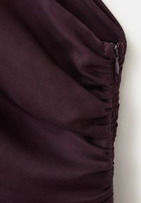 Tissu violet foncé avec des détails froncés et une fermeture éclair fermée le long du bord, montrant la texture et les coutures.