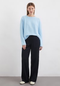 Un pull bleu clair à manches longues avec un col rond, associé à un pantalon large noir et des chaussures à enfiler crème. Design simple et épuré.