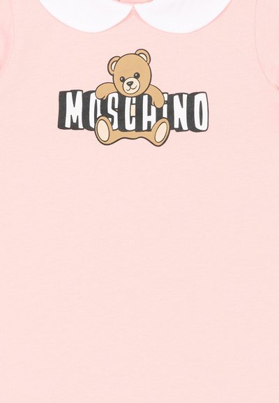 Pink beklædningsgenstand med hvid krave, der har en tegneserie-bamse siddende over fed sort og hvid tekst, der staver "MOSCHINO."