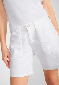 Witte denim shorts met een hoge taille, twee frontzakken en een enkele knoopsluiting. De stof is glad met een lichte textuur.