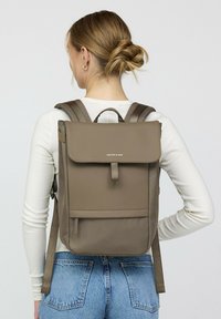 Bruine stoffen rugzak met een klep sluiting, verstelbare schouderbanden en een voorvak. Soepele textuur en minimalistisch ontwerp.