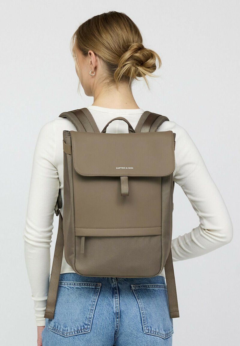 Bruine stoffen rugzak met een klep sluiting, verstelbare schouderbanden en een voorvak. Soepele textuur en minimalistisch ontwerp.