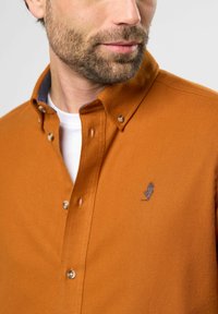Polohemd van oranje stof, met een gestructureerde kraag, contrasterende binnenkraagvoering en een klein geborduurd logo op de borst.