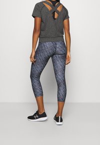 Harmaa urheilupaita, jossa on ristikkäiset selkäremmit, yhdistettynä sinisiin legginsseihin, joissa on toistuvia vaaleanharmaita logoja ja mustiin lenkkareihin.