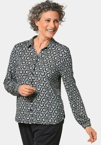 Langarm blouse met een zwart-wit geometrisch patroon, voorzien van een kraag en knoopsluiting, gemaakt van lichtgewicht stof.
