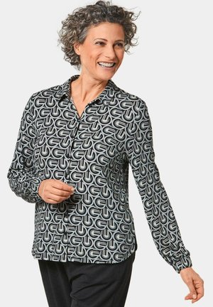 Long-sleeve blouse featuring a black and white geometric pattern, with a collared neckline and button closure, made from lightweight fabric.