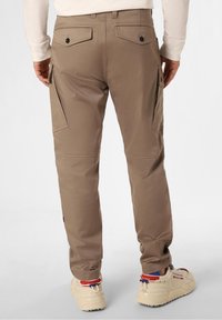 Béžové cargo kalhoty s dvojitými bočními kapsami, kapsami na zadní straně s knoflíkovými zapínáními, na míru střižené a s jemným leskem. Nošeny s béžovými teniskami.