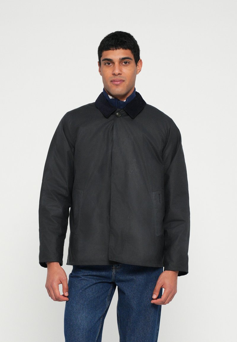 Casaco preto com gola em azul escuro, com fecho de botões na frente e dois bolsos laterais. O tecido aparenta ser suave com textura mínima.