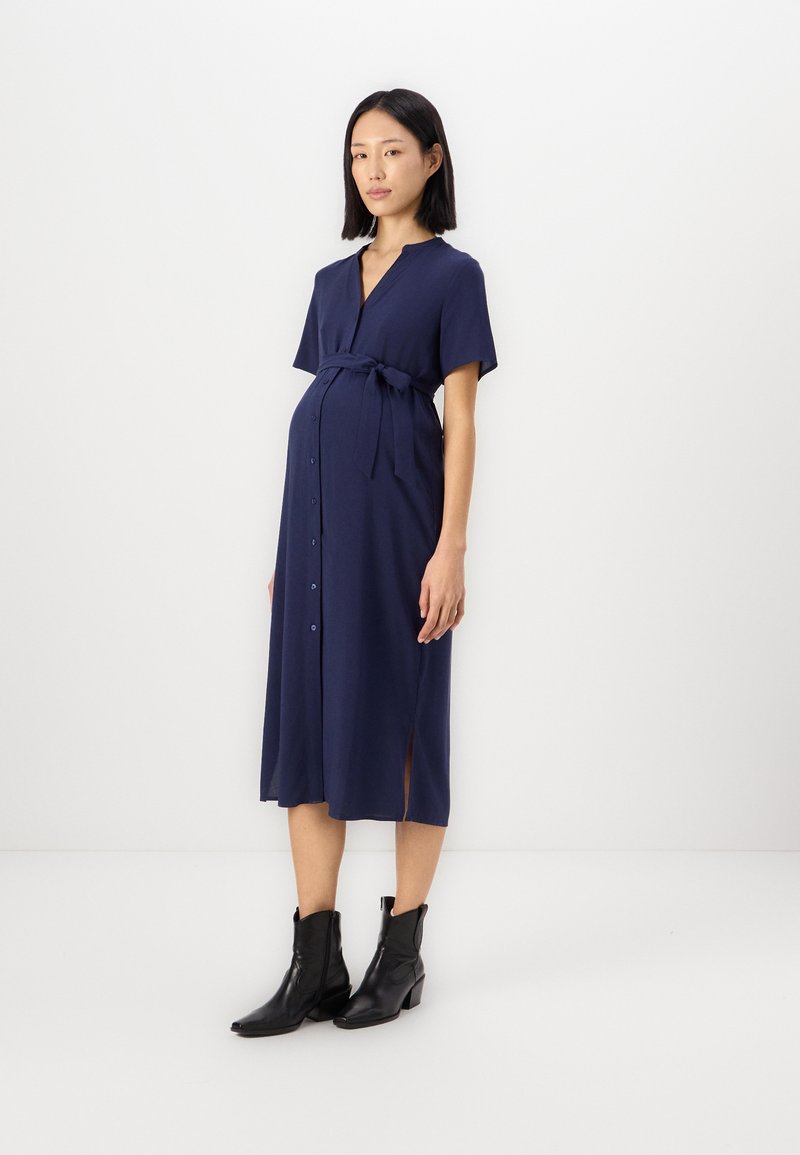 Ναυτικό φόρεμα εγκυμοσύνης με κοντά μανίκια, κουμπιά μπροστά και πλαϊνές σχισμές, διαθέτει ζώνη στο μέσο και λείο ύφασμα.