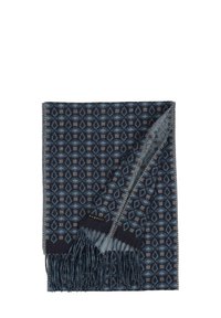Couverture bleu foncé à motifs géométriques, avec des bords frangés et une texture douce. Une étiquette avec le nom de la marque "bugatti" est visible.