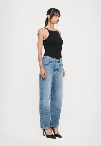 Top de alças finas preto canelado, combinado com jeans de perna larga de cintura alta azul claro e sapatos de salto fino pretos.