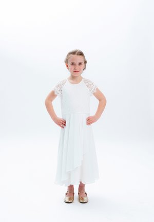 Weißes Kleid mit kurzen Spitzenärmeln, gestuftem Rock und strukturiertem Oberteil. Kombiniert mit glänzenden goldenen Ballerinas. Einfaches, elegantes Design.