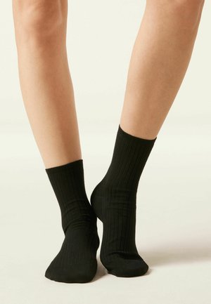 Calcetines negros acanalados de longitud media, con una textura suave y aberturas elásticas para un ajuste ceñido.