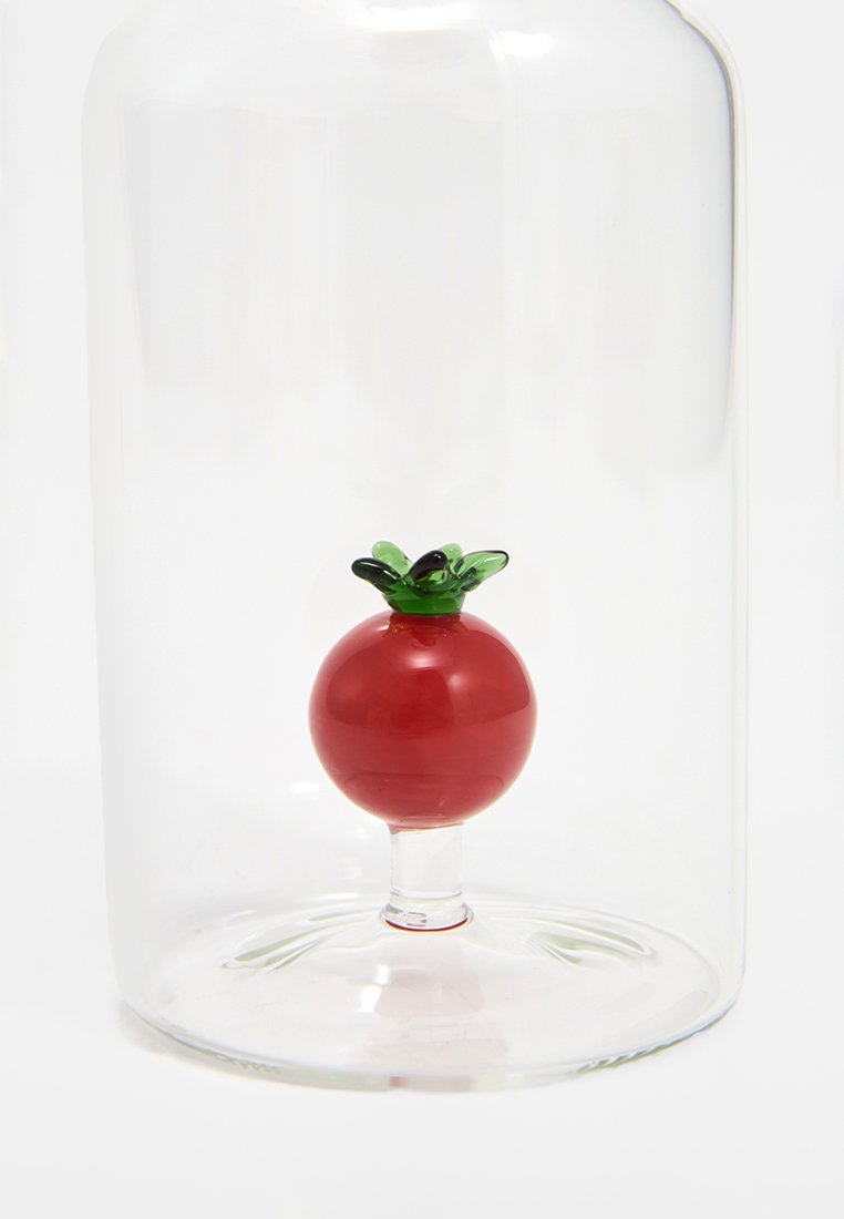 Mały czerwony szklany pomidor z zielonymi liśćmi wewnątrz przezroczystej, klarownej szklanej kopuły na białym tle.