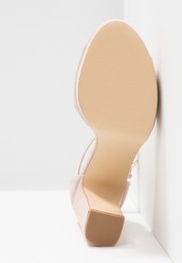 Chaussure à talon haut beige en daim doux, avec un bout pointu et une semelle en caoutchouc texturée, présentée en angle sur un fond neutre.