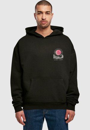 Sort hættetrøje med en frontlomme, der har et grafisk motiv af en pink sol med stråler og bølger, mærket "SUNSET CHARM." Tykt stof, løst fit.