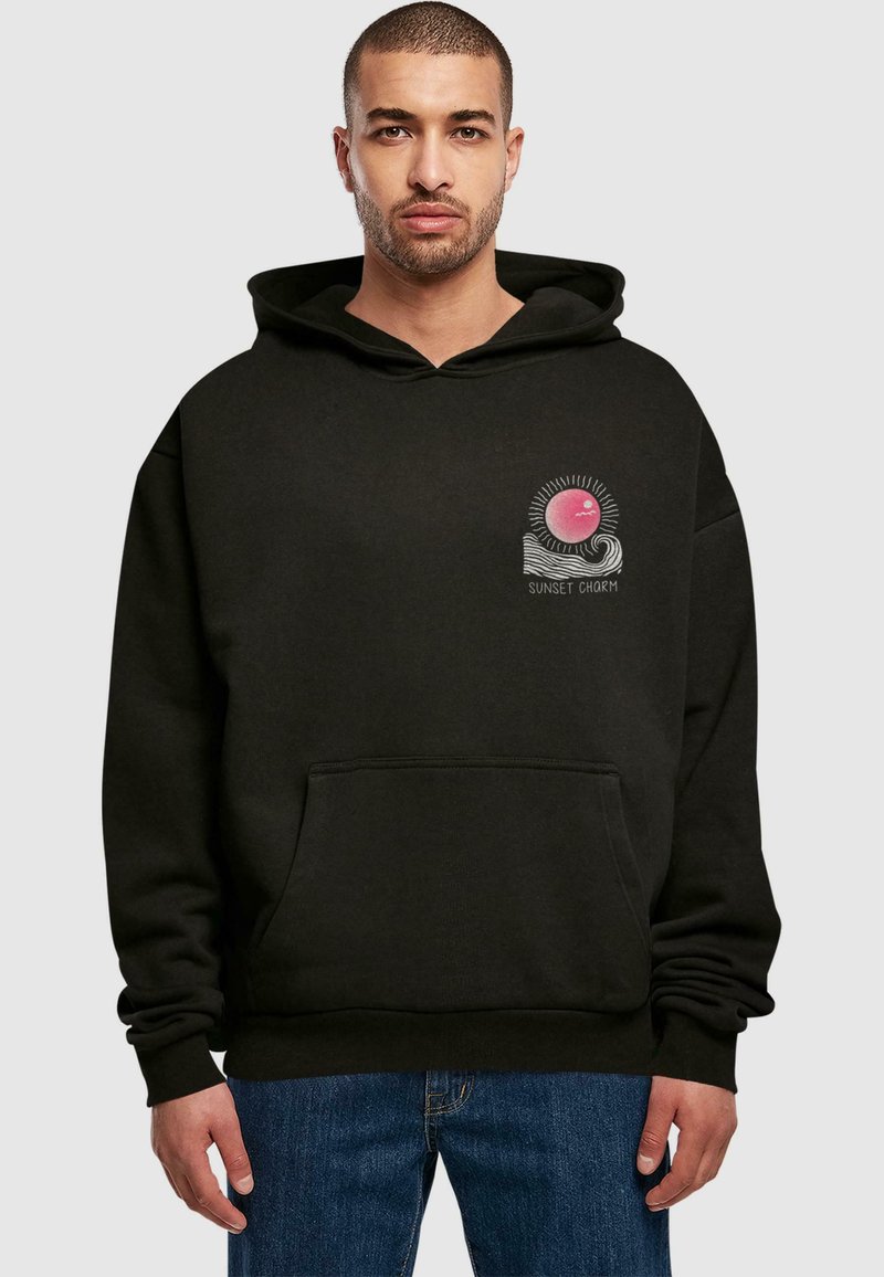 Felpa nera con tasca frontale, caratterizzata da una grafica di un sole rosa con raggi e onde, etichettata "SUNSET CHARM". Tessuto spesso, vestibilità ampia.